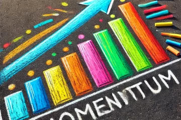 A chalk drawing on asphalt depicting a bar graph with increasing colorful bars and an upward arrow labeled 'Momentum'. The bars are in bright colors such as blue, yellow, orange, pink, and green, and the arrow points upwards to the right, symbolizing growth and progress.